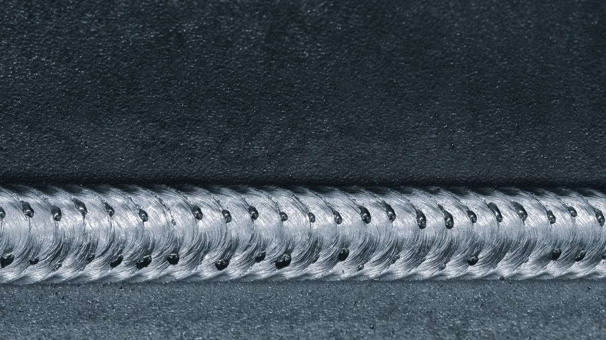 Close-up of a metal part with a finished weld seam resting on a production table